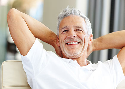 Man in white t-shirt relaxing on a sofa happy with his new dentures